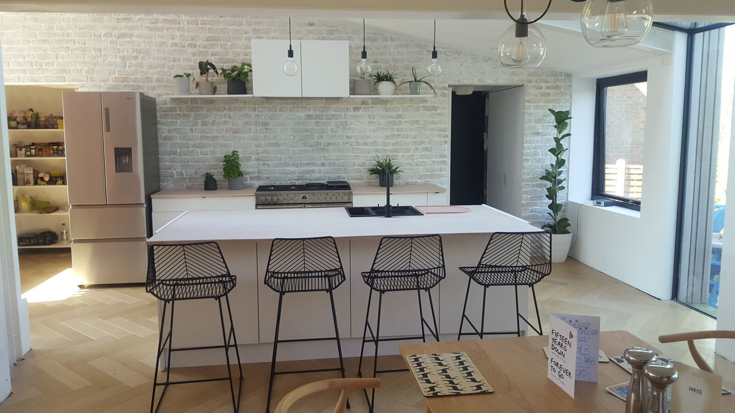 Modern kitchen with a whitewashed brick slip feature wall, minimalist decor, and sleek black bar stools. A perfect blend of contemporary and rustic design.